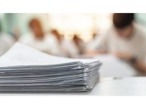 Photo d'une pile de feuille avec élèves en arrière plan.