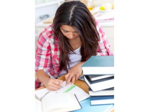 Photo d'une étudiante qui écrit avec une pile de livres à ses côtés.
